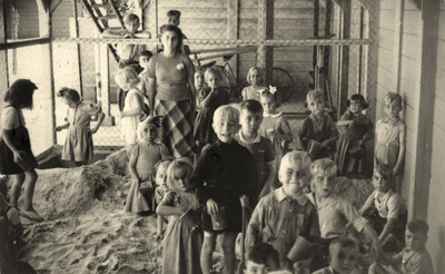 604973 Afbeelding van een groep kinderen met een onderwijzeres in de overdekte zandbak achter de Van Alphenschool ...